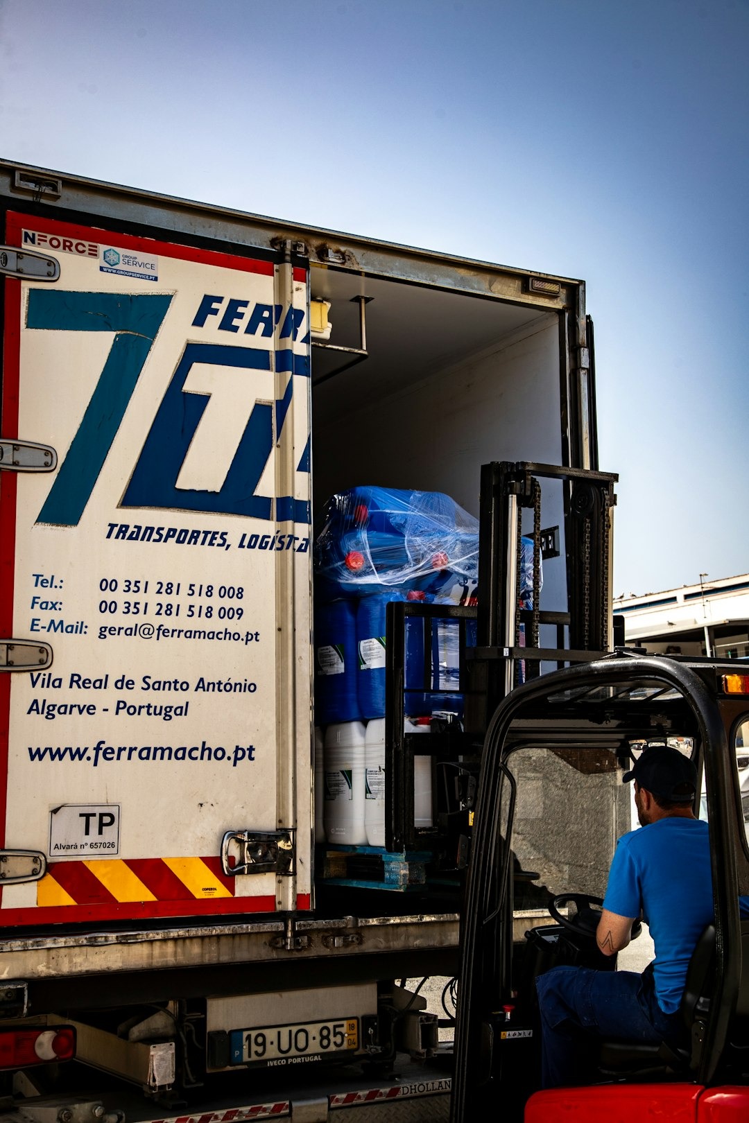 Logistics worker loading industrial barrels onto a delivery truck.